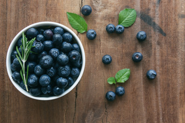 Fresh ripe wild blueberries in white bowl on rustic wood table in top view flat lay with copy space for background. Blueberry is antioxidant food and vitamin C. Healthy and delicious fruits concept.