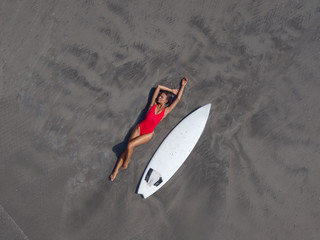 Surf girl in a red swimsuit on the beach with a surfboard