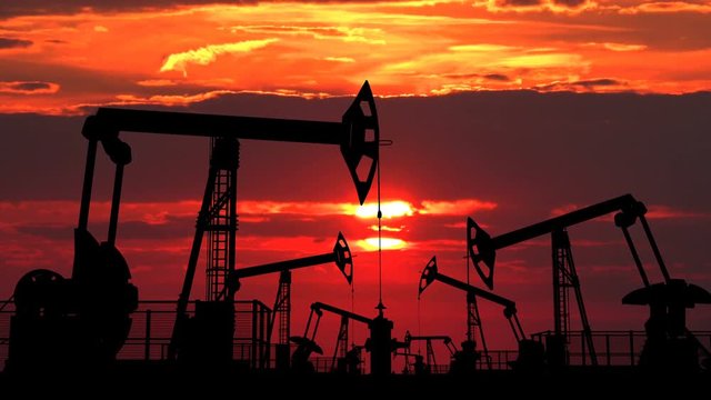 Fielld of oil pumpjacks against red evening cloudscape