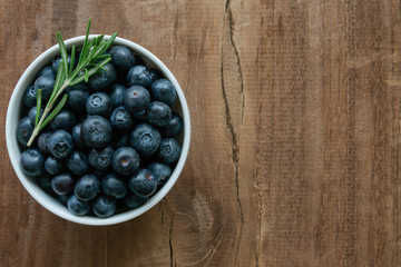 Fresh ripe wild blueberries in white bowl on rustic wood table in top view flat lay with copy space for background. Blueberry is antioxidant food and vitamin C. Healthy and delicious fruits concept.