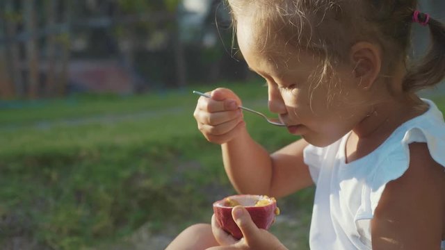 Close-up of cute little girl eating a passionfruit outdoor in slow motion