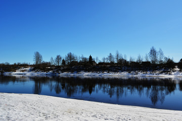 Fototapeta na wymiar beautiful spring natural landscape sunny day, river among the snow-capped coasts against the blue sky, reflection of trees in the water, nature countryside