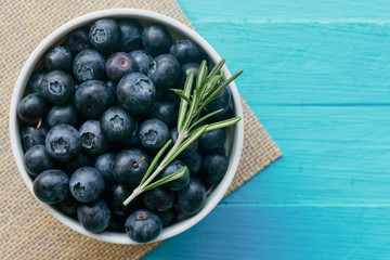 Fresh ripe wild blueberries in white bowl on blue wood table in top view flat lay with copy space for background. Blueberry is antioxidant food and vitamin C. Healthy and delicious fruits concept.
