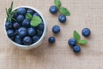Fresh ripe wild blueberries in white bowl on rustic sack in top view flat lay with copy space for background. Blueberry is antioxidant food and vitamin C. Healthy and delicious fruits concept.