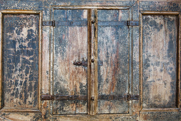 Close up outdoor view of part of ancient closed wooden shutters. Detail of rusty metallic hinges fixed with several screws. Grey painted surface. Pattern with vertical planks and separation lines.