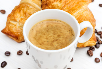 Cup of coffee, two croissants and coffee beans on the table. Top view.