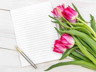 Blank notepad and bouquet with tulips on the wooden table. Top view.