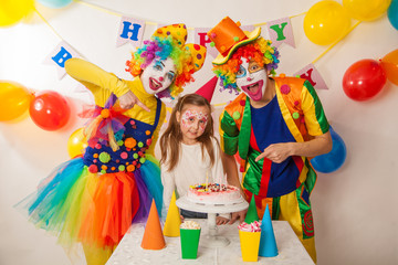 clown girl and clown boy at the children's birthday party. Festive table with a beautiful cake. Blow out candles and make a wish