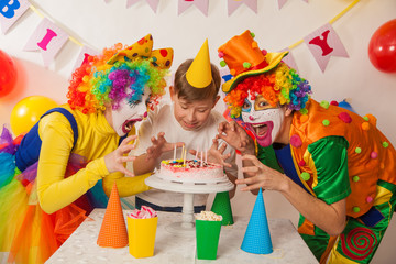 clown girl and clown boy at the birthday party of an adult guy. Festive table with a beautiful cake. Blow out candles and make a wish