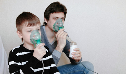 Use nebulizer and inhaler for the treatment. Man and boy inhaling through inhaler mask. Side view.