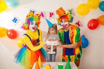 Obraz na płótnie Canvas clown girl and clown boy at the birthday of a little girl. Festive table with a beautiful cake. Blow out candles and make a wish
