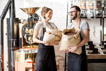 Portrait of a two happy baristas in uniform standing with bags full of coffee beans at the coffee store