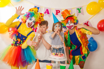 clown girl and clown boy at the birthday of a little girl and her big brother. Festive table with a beautiful cake. Blow out candles and make a wish