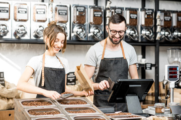 Two sellers in uniform filling bags with coffee beans while working in the coffee store