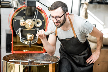 Man checking the quality of the coffee beans standing with scoop near the roaster machine at the roastery