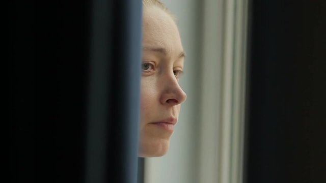 Close-up of a woman's face peeping out from behind the curtains