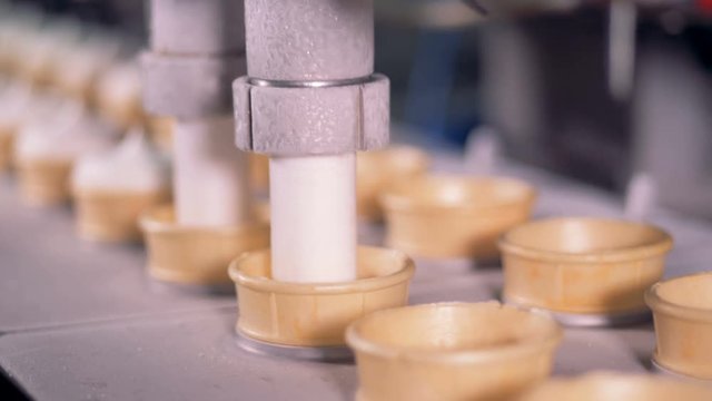 Wafer cups are getting filled with ice-cream paste by a factory machine