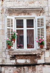 Fototapeta na wymiar Windows and flower boxes of historical building from old town of Pula, Croatia / Detail of ancient venetian architecture with decorative element / Building material, texture, background and wallpaper.