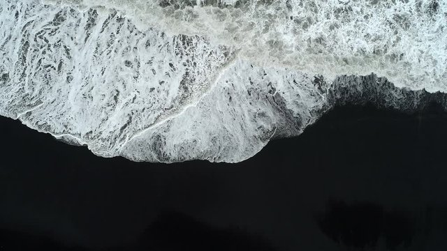 Aerial footage of waves breaking against black sand beach in Iceland.