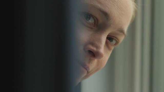 Close-up of a woman's face peeping out from behind the curtains