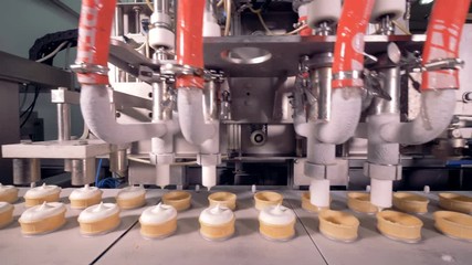 Four industrial pipes are filling moving wafer cups with ice-cream substance 
