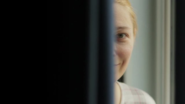 Close-up of a woman's face peeping out from behind the curtains