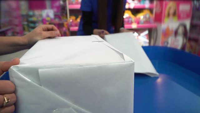 Young woman wrapping Christmas presents with white paper in a toy store