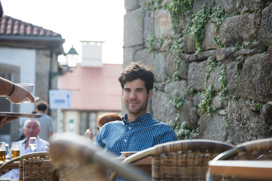 Man sitting on outdoor terrace being served a cup of coffee