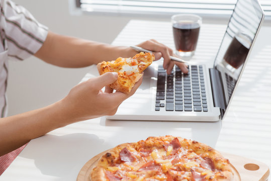 close up man hand eating pizza while working in laptop computer