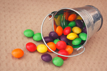 Colorful candies in metallic bucket spilled on textile background