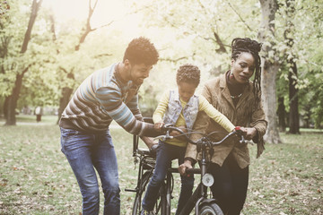 Happy African American parents teaching their little girl to driving bike in park.