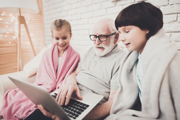 Obraz premium Grandfather, grandson and granddaughter at home. Grandpa and children are watching movie on laptop.