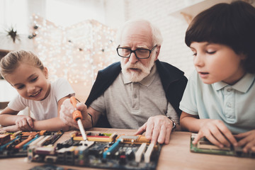 Grandfather, grandson and granddaughter at home. Grandpa teaches children how to braze.