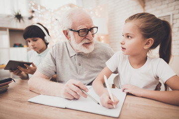 Fototapeta premium Grandfather, grandson and granddaughter at home. Grandpa is helping girl with homework.