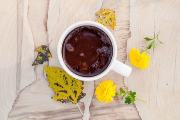 Autumn background cup of coffee with yellow flowers and autumn leaves on a wooden background.