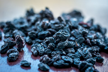 Black raisin or kali kishmish or Zante currant in a white plate on wooden surface in dark Gothic...