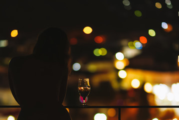 Silhouette of naked woman on the balcony with a glass of wine on the background of a night city