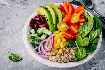 Healthy vegan lunch Buddha bowl. Avocado, quinoa, tomato, cucumber, red beans, spinach, red onion and red paprika vegetables salad.