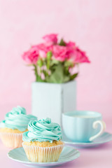 Cupcake with sweet mint cream decoration and bouquet of red roses in retro shabby chic vase on pink pastel background.