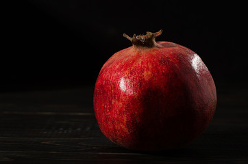 one ripe pomegranate on a black wooden background