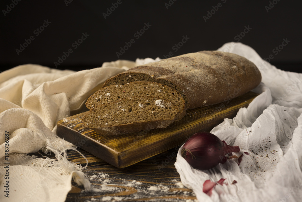 Wall mural Conceptual still life of pieces of bread and two onion bulbs, on an ancient wooden table lying on a wooden tray, a piece of cloth