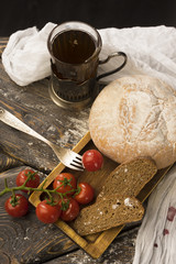 Conceptual still life of sliced bread, cherry tomatoes, glass of tea and vintage fork, on an ancient wooden table, and a piece of cloth