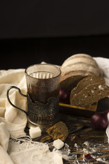 Conceptual still life of pieces of bread, onion bulb, a glass of tea and refined sugar, on an ancient wooden table lying on a wooden tray, a piece of cloth