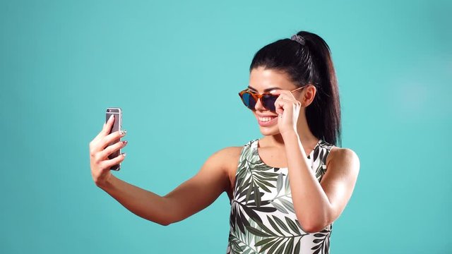 Beauty playful brunette woman in dress and glasses posing and making selfie on her smartphone.
