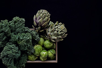 fresh green vegetables in wooden basket on black background 