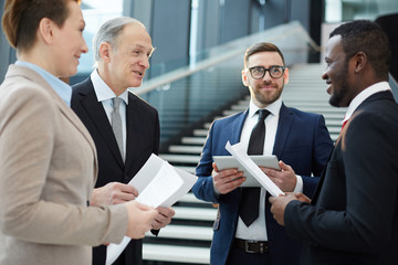 Group of intercultural business partners or delegates in suits discussing their ideas for reports before conference