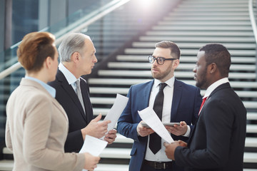 Group of colleagues of various ages and ethnicities gathered for working meeting to discuss details of their reports