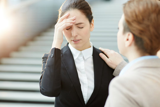 Young businesswoman touching her head and expressing that she forgot something while colleague saying it is okay