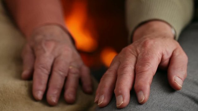 Senior hands of woman and man resting at the fireplace - old age concept, closeup, shallow depth, camera dolly