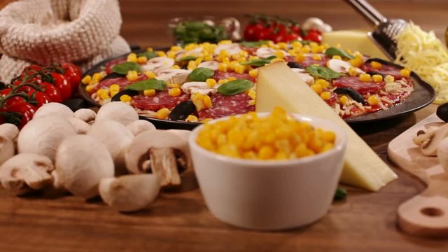 Camera moves around a homemade delicious pizza in round pan with ingredients on the side - closeup, focus on pizza, low angle